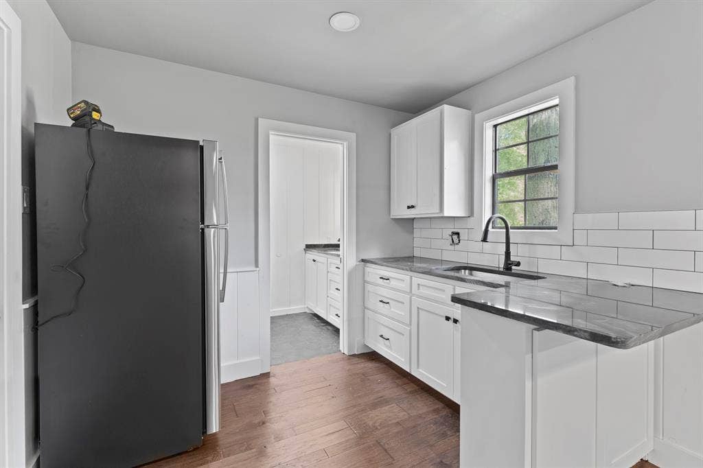 18630 Eastside Road, Troup, TX 75789 Kitchen featuring wood-finish flooring, white cabinetry with dark hardware, dark countertops, and a white subway tile backsplash
