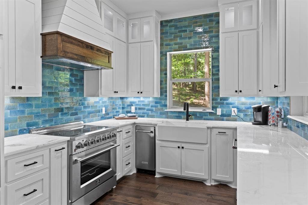 18630 Eastside Road, Troup, TX 75789 White shaker cabinetry, blue subway tile backsplash, farmhouse-style sink, stainless steel range, and wood-finish flooring
