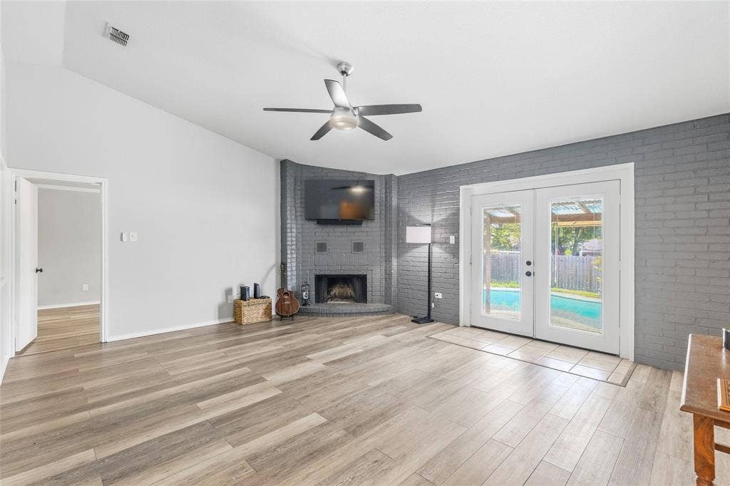 5010 Utah Street, Greenville, TX 75402 Vaulted ceiling with a ceiling fan, corner brick fireplace, wood-finish flooring, and French doors opening to a pool