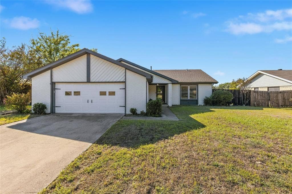 5010 Utah Street, Greenville, TX 75402 White brick exterior with a gray roof and trim, an attached garage with decorative hardware, a concrete driveway, and a front lawn