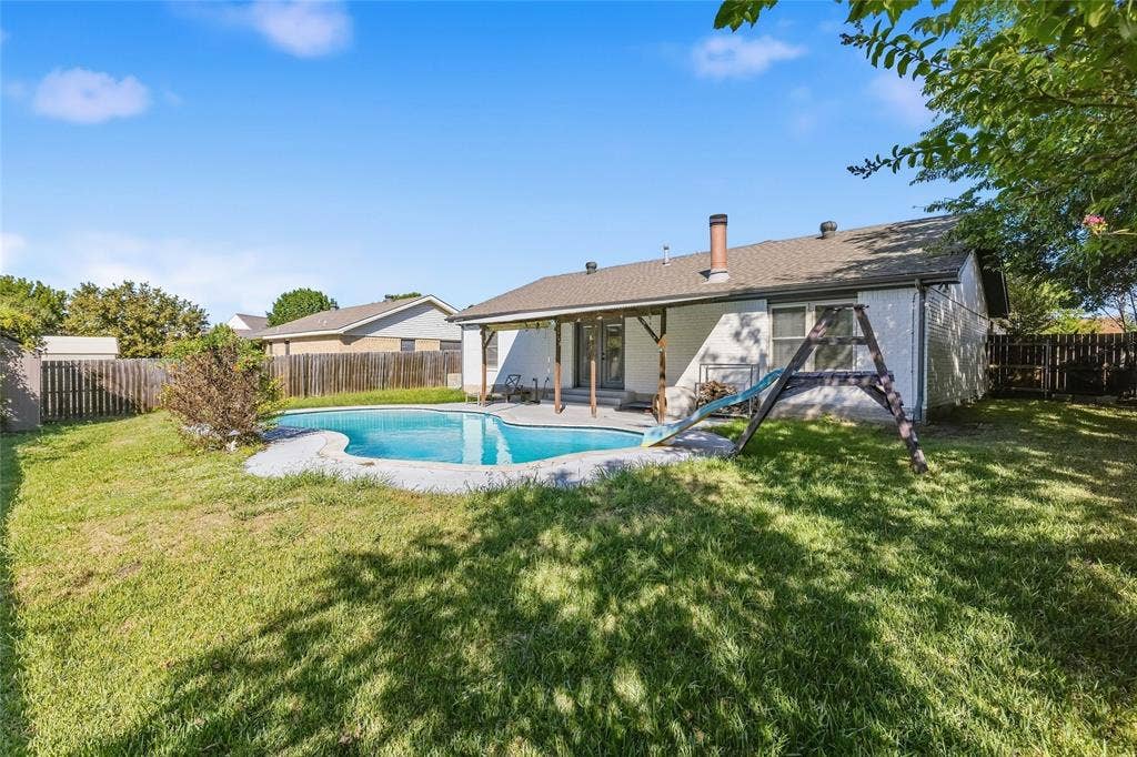 5010 Utah Street, Greenville, TX 75402 Expansive backyard featuring a built-in swimming pool with a surrounding paved deck, a covered patio with exposed wood beams, and a wood privacy fence