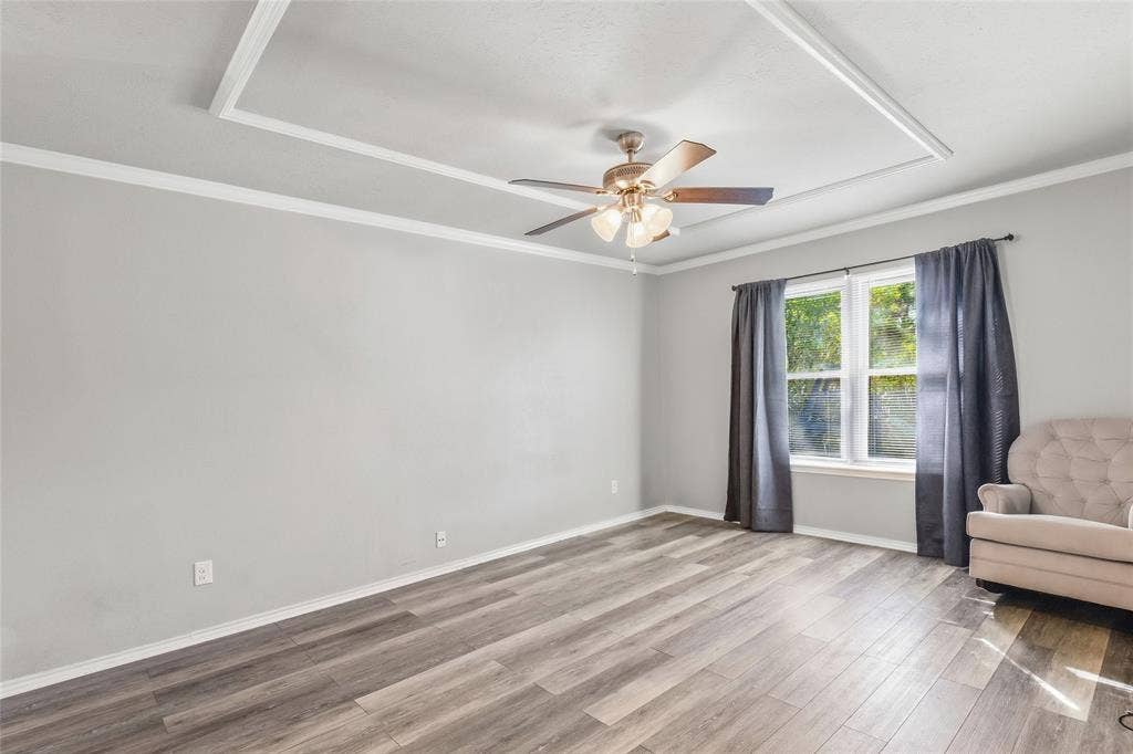 5010 Utah Street, Greenville, TX 75402 Wood-finish flooring, tray ceiling with crown molding, ceiling fan with light fixture, and window with trim