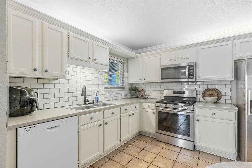 5010 Utah Street, Greenville, TX 75402 White shaker-style cabinetry with crown molding, stainless steel appliances, subway tile backsplash, dual basin stainless steel sink, and light-toned countertops