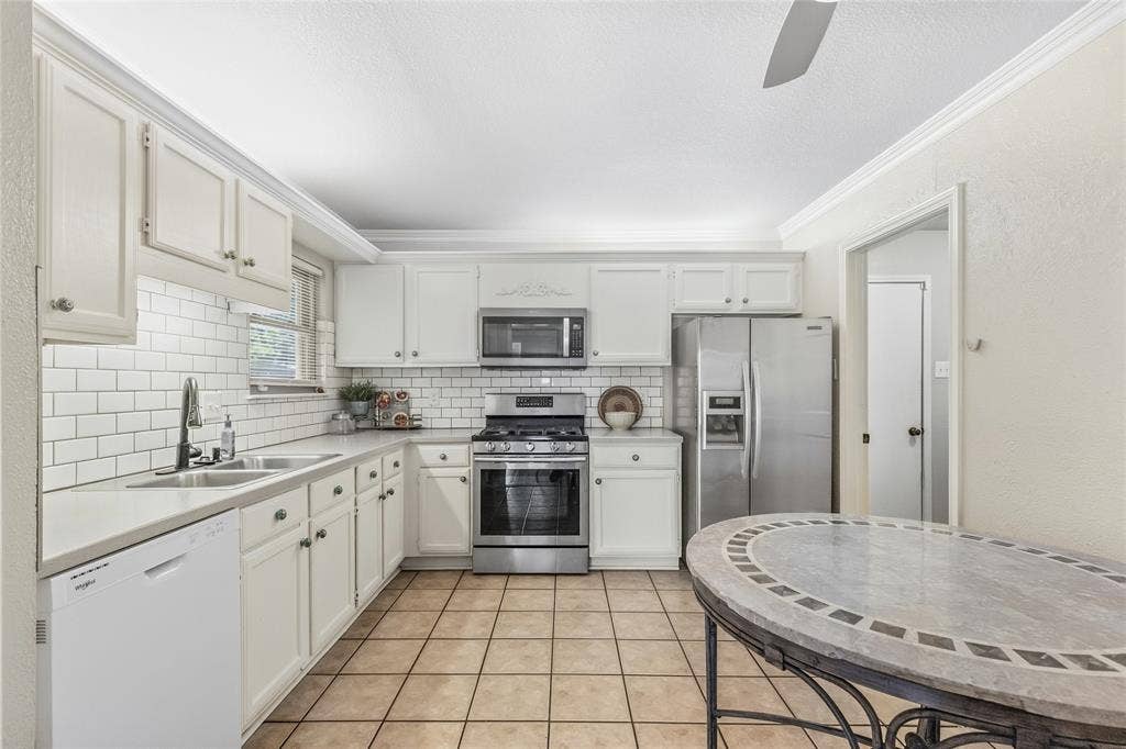 5010 Utah Street, Greenville, TX 75402 White cabinetry with crown molding, subway tile backsplash, stainless steel appliances, and tile flooring
