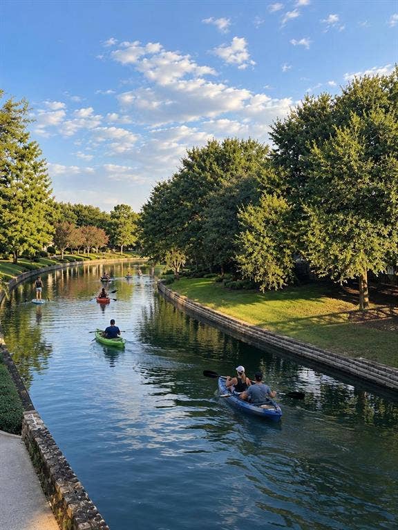 308 Riverwalk Lane, Irving, TX 75063 Waterway access featuring a stone-clad retaining wall, paved walkway, and verdant landscaping