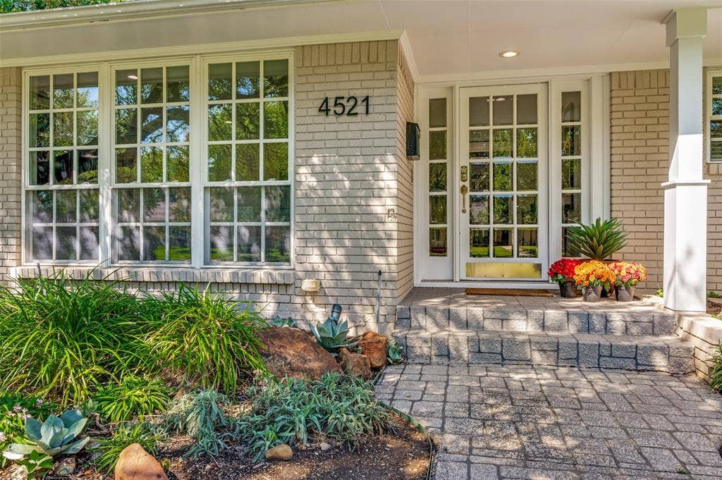 4521 Nashwood Lane, Dallas, TX 75244 Light-colored brick exterior with multiple windows, a glass-paned front door, and a stone-tiled entryway