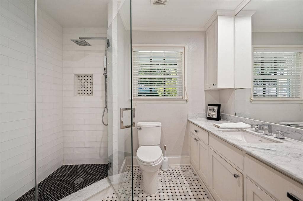 4521 Nashwood Lane, Dallas, TX 75244 Shower with glass enclosure and rain-style showerhead, mosaic tile flooring, white subway tile shower walls, marble vanity with built-in cabinetry, and marble-finish countertop