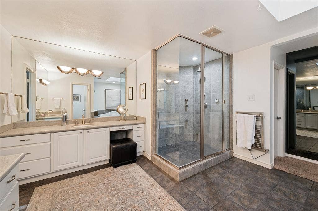 4521 Nashwood Lane, Dallas, TX 75244 Glass-enclosed shower with a built-in bench, dual vanity with white cabinetry, large wall-mounted mirror, and tile flooring