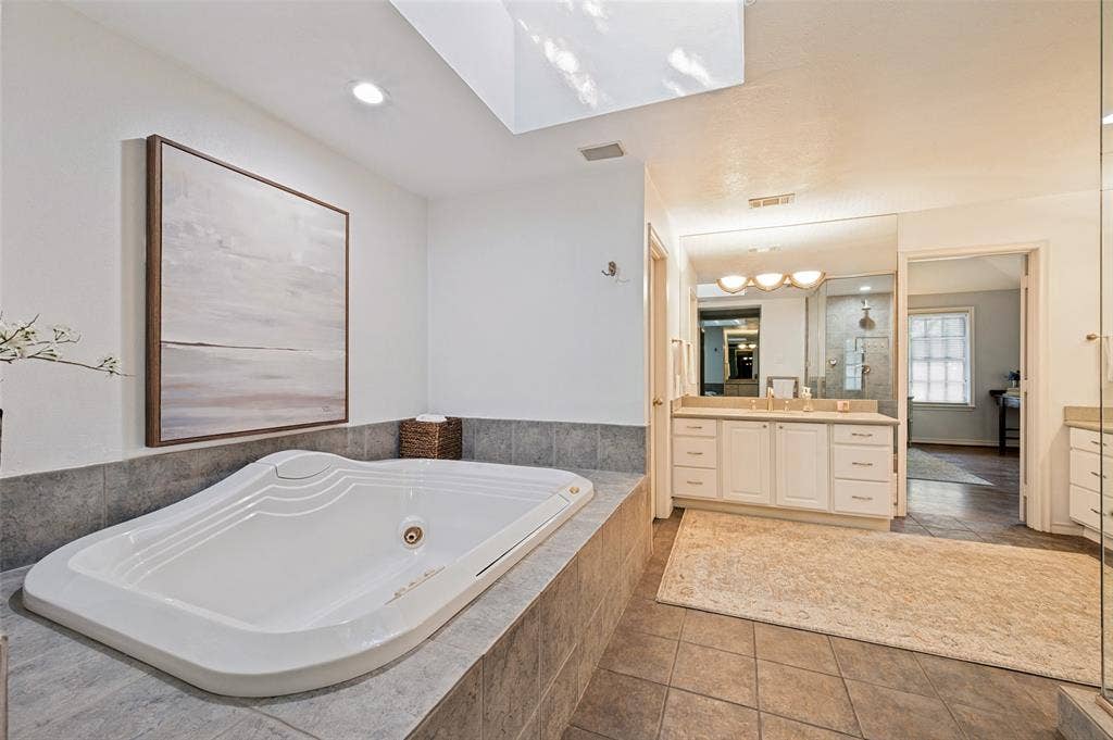 4521 Nashwood Lane, Dallas, TX 75244 Soaking tub with tiled surround, dual vanity with undermount sinks, and a large mirror with integrated lighting