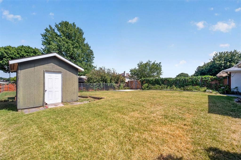 1101 Boyd Drive, Wylie, TX 75098 Expansive lawn area featuring a storage shed with a white door, established trees, and perimeter fencing