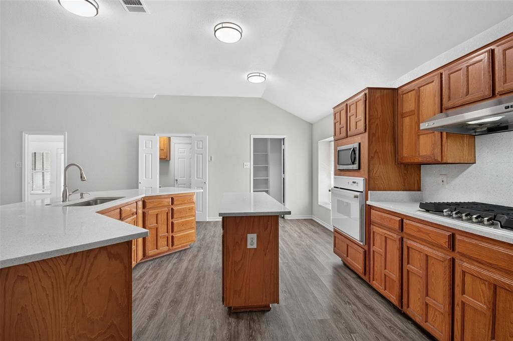 1101 Boyd Drive, Wylie, TX 75098 Kitchen featuring wood-finish cabinetry, light-toned countertops, a stainless steel gas range, and a built-in oven with a microwave