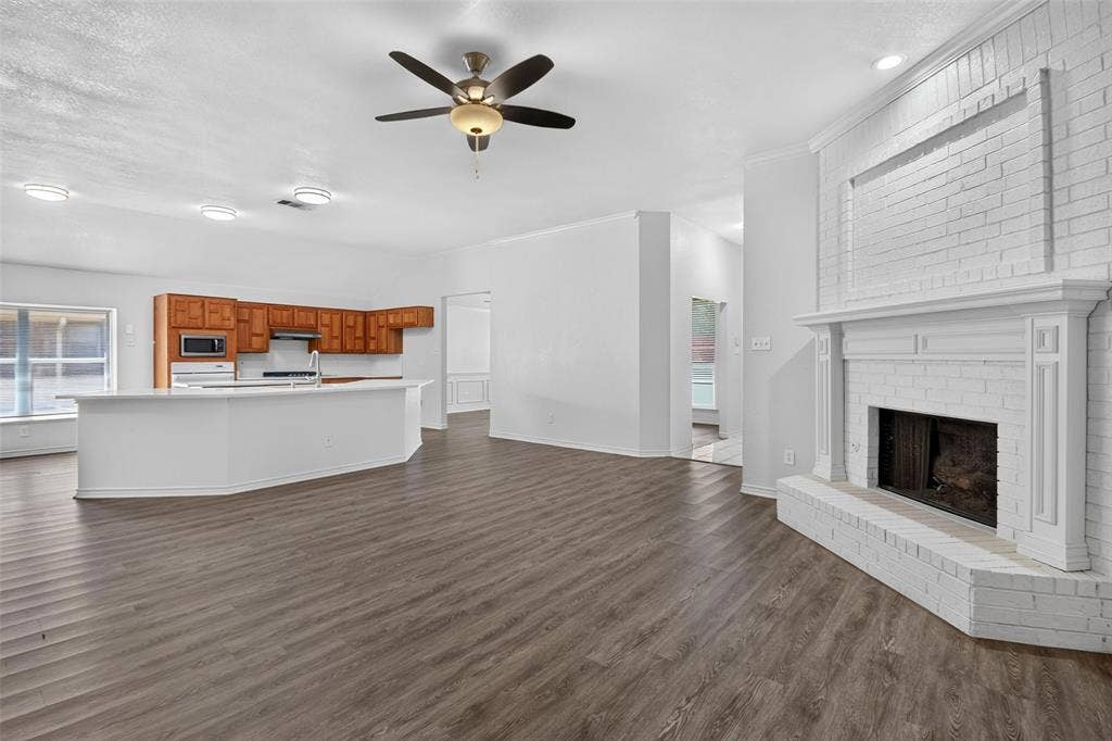 1101 Boyd Drive, Wylie, TX 75098 Spacious living area featuring wood-finish flooring, a white-painted brick fireplace with a mantle, and an open-concept kitchen with wood cabinetry and a central island