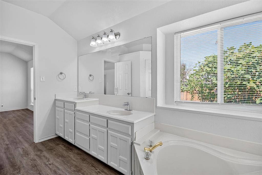 1101 Boyd Drive, Wylie, TX 75098 Dual vanity with undermount sinks and chrome fixtures, large integrated mirror, recessed soaking tub with gold-tone fixtures, and window with horizontal blinds
