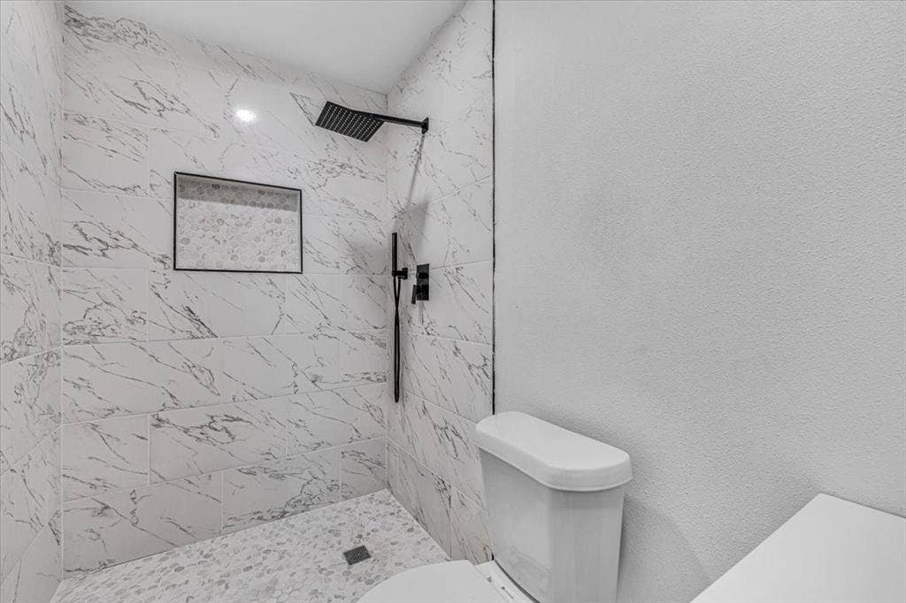 13521 Flagstone Lane, Dallas, TX 75240 Tiled shower with matte black fixtures, an integrated shower niche, and a contrasting pebble-style shower floor