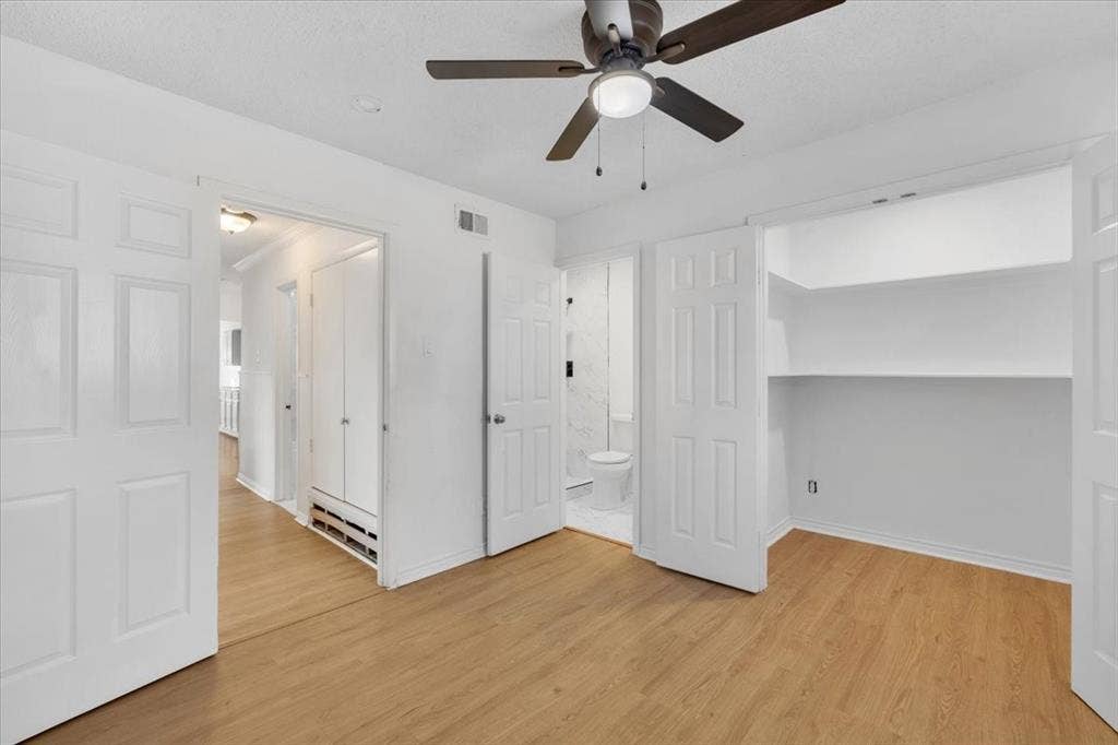 13521 Flagstone Lane, Dallas, TX 75240 Wood-finish flooring, ceiling fan with integrated lighting, built-in shelving, white paneled doors, and a partial bathroom with a toilet and tiled walls