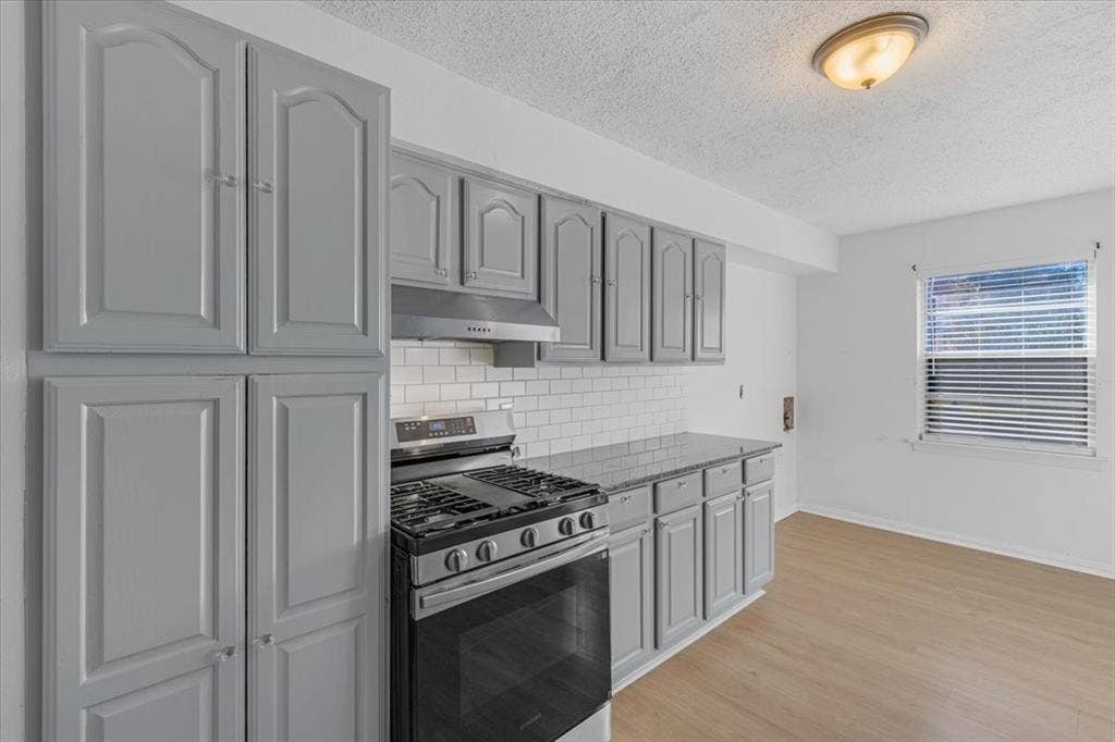 13521 Flagstone Lane, Dallas, TX 75240 Gray cabinetry with silver hardware, stainless steel range and hood, white subway tile backsplash, light wood-finish flooring, and a flush mount ceiling light