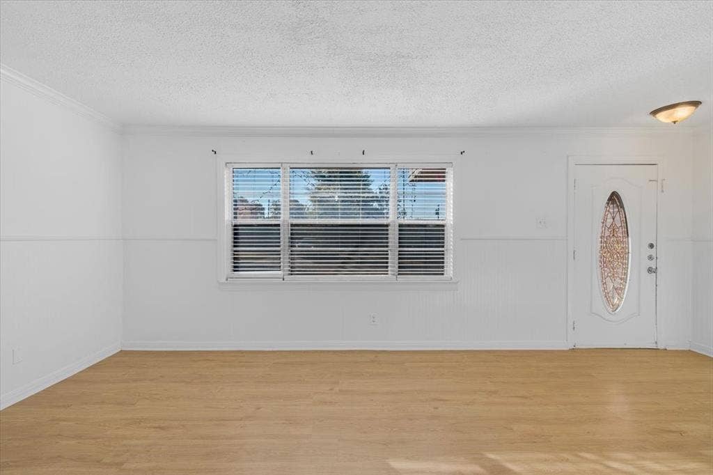 13521 Flagstone Lane, Dallas, TX 75240 White interior walls, crown molding, wood-finish flooring, white entry door with decorative glass inlay, and a flush mount ceiling light