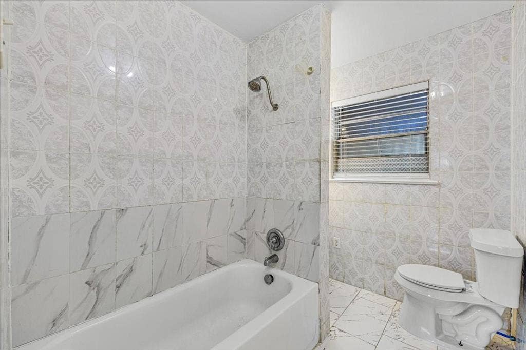 13521 Flagstone Lane, Dallas, TX 75240 White ceramic bathtub with a shower fixture, white toilet, and patterned tile walls and flooring