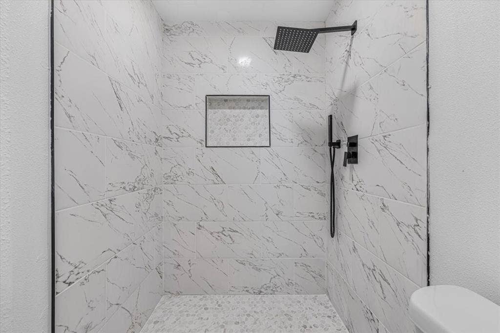 13521 Flagstone Lane, Dallas, TX 75240 Walk-in shower featuring large format wall tile, a mosaic tile shower pan, a built-in shower niche, and matte black shower fixtures