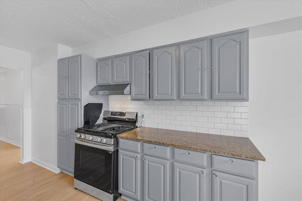 13521 Flagstone Lane, Dallas, TX 75240 Stainless steel range with coordinating hood, white subway tile backsplash, light wood-finish flooring, grey cabinetry, and stone-finish countertops