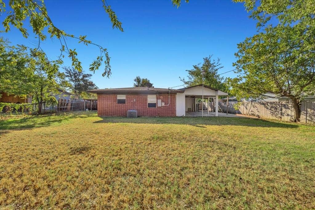 13521 Flagstone Lane, Dallas, TX 75240 Expansive backyard with a covered patio, brick exterior, fenced perimeter, and mature trees