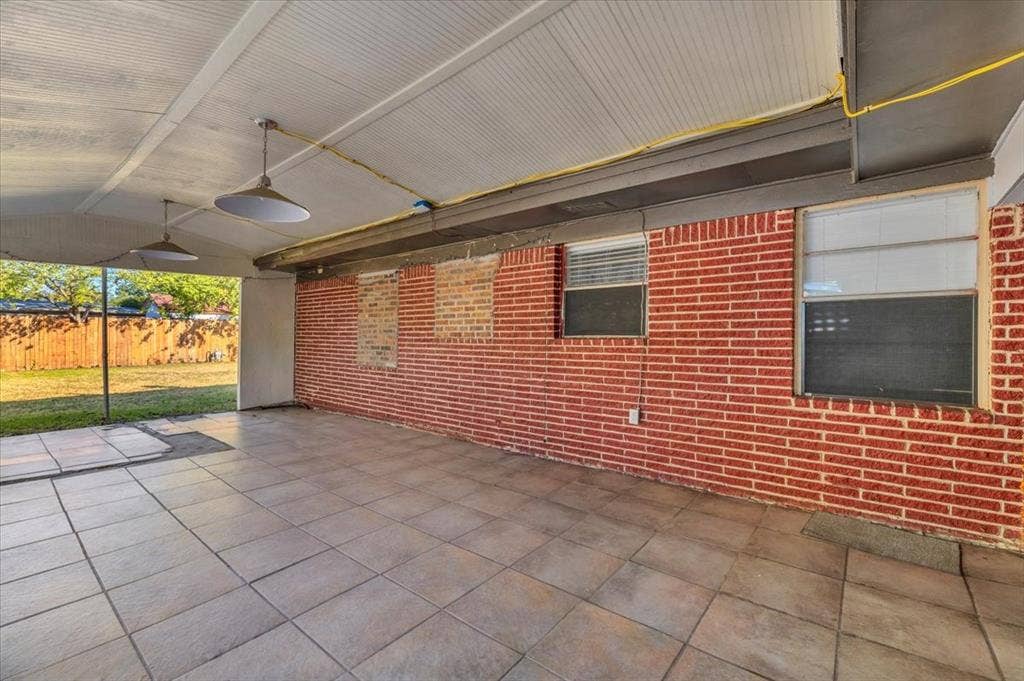 13521 Flagstone Lane, Dallas, TX 75240 Covered patio featuring a tiled floor, brick wall, two pendant light fixtures, and a wood privacy fence