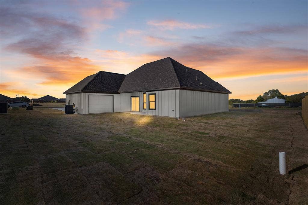 Rear exterior featuring a spacious lawn, board and batten siding, dark shingled roof, and an attached garage with a roll-up door
