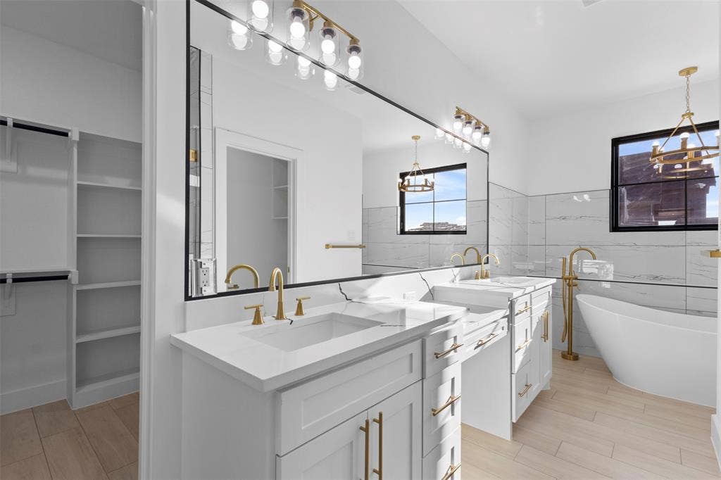 Dual vanities with white countertops, gold-finish fixtures, and a large mirror with integrated lighting
