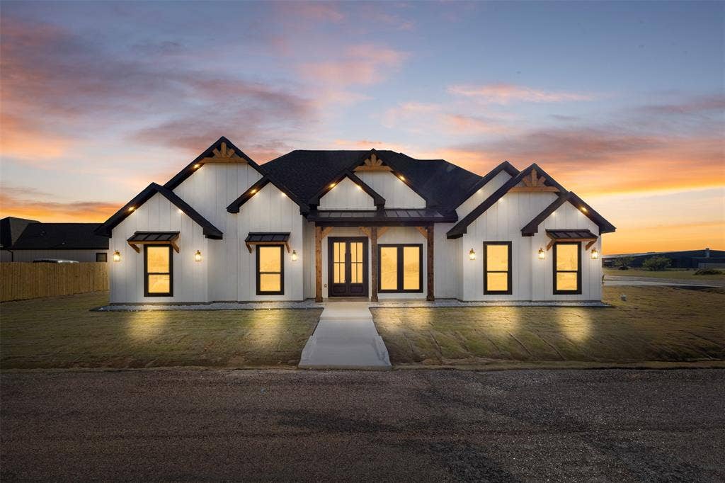 Modern farmhouse exterior with white vertical siding, black-framed windows, dark roofing, and exposed wood architectural accents