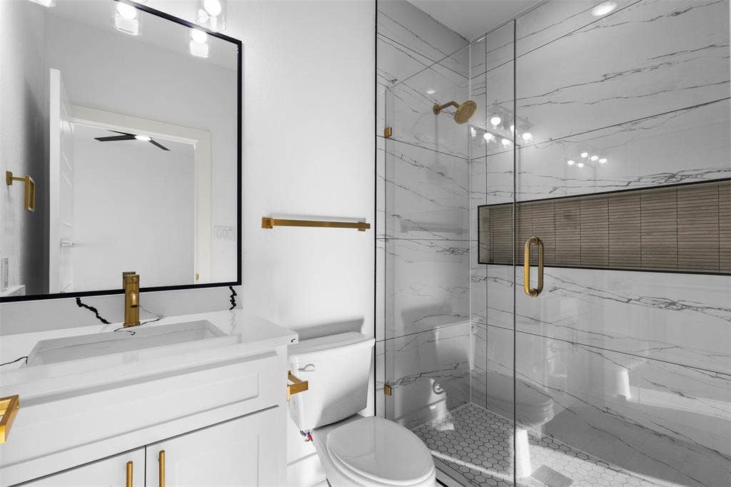 Glass-enclosed shower with a recessed niche, white hex-tile shower pan, and gold-finish fixtures