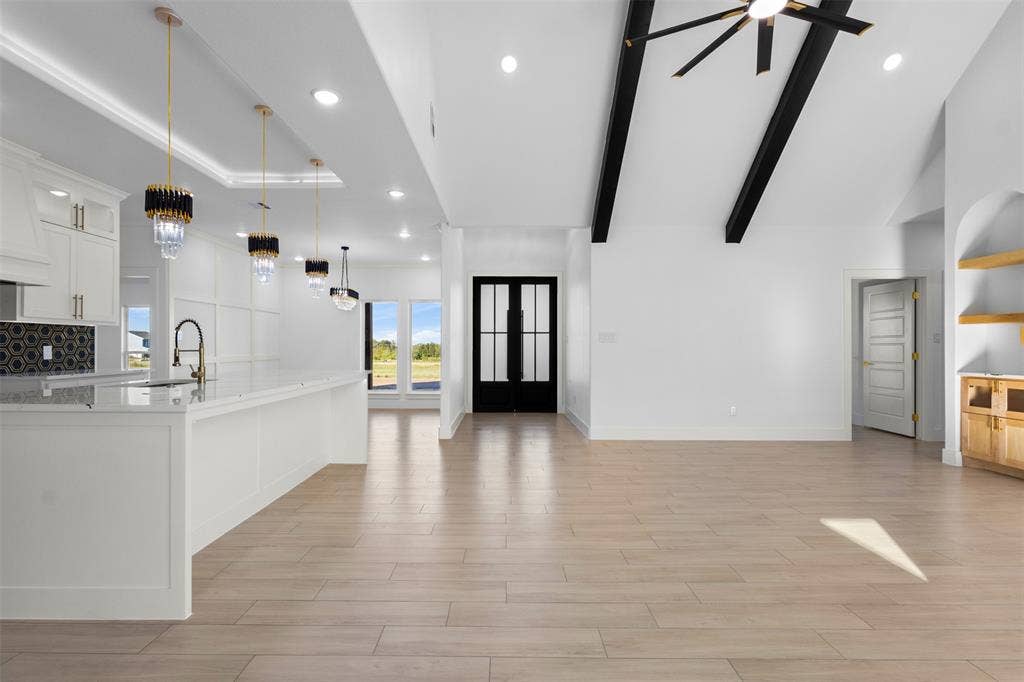 Vaulted ceiling with exposed beams, wood-finish flooring, built-in shelving, white cabinetry, and a kitchen island with pendant lighting