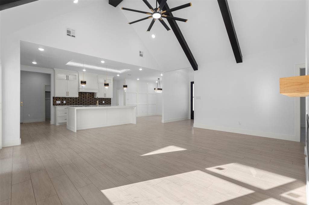 Vaulted ceiling with exposed beams, wood-finish flooring, recessed lighting, kitchen island, and built-in cabinetry