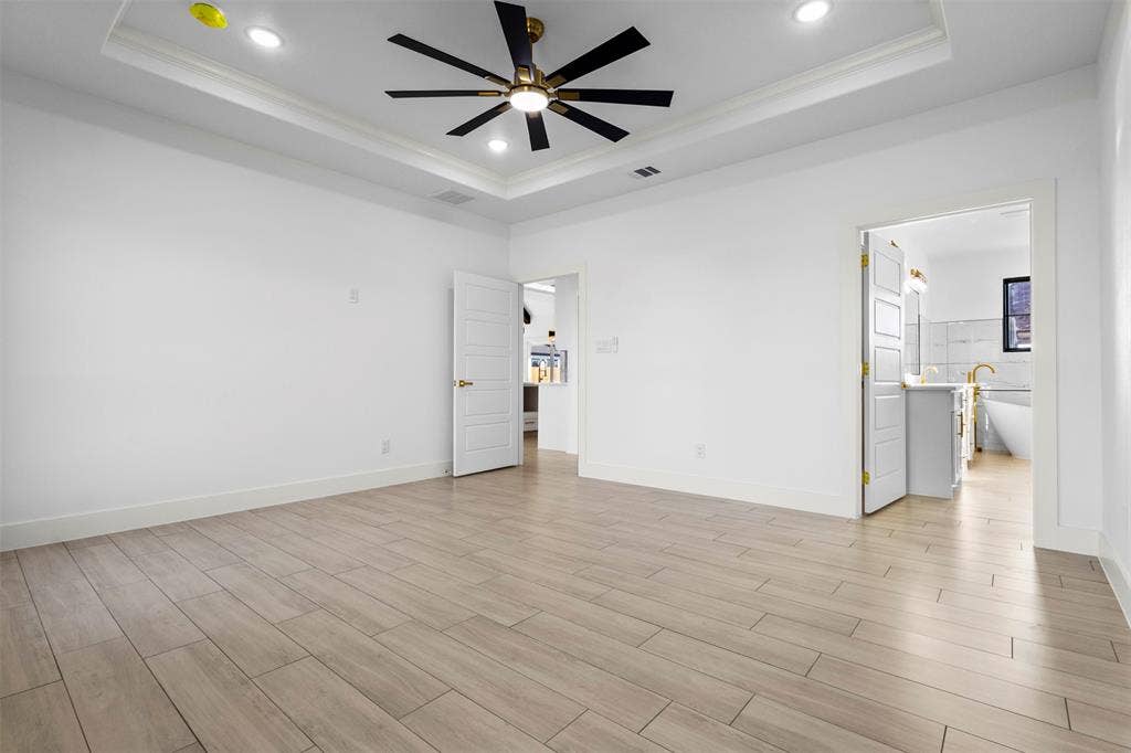 Tray ceiling with recessed lighting, ceiling fan with black blades, white paneled doors, and wood-finish tile flooring