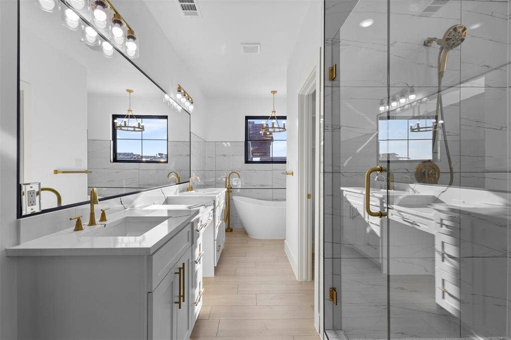 Dual vanities with white countertops, gold-finish fixtures, and a large frameless mirror