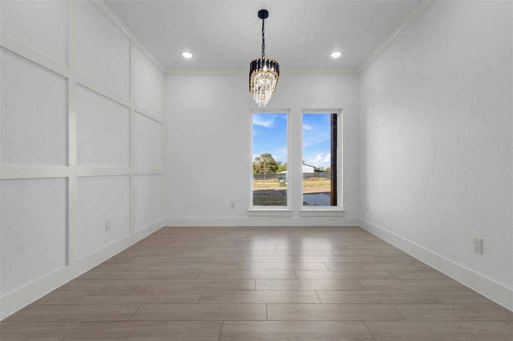 Recessed lighting, elegant chandelier, wood-finish flooring, two large windows, and a decorative paneled accent wall