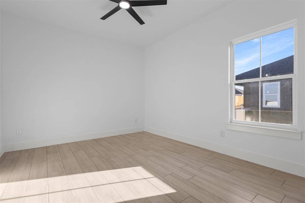 White walls, wood-finish flooring, white window trim, and a black ceiling fan with integrated lighting
