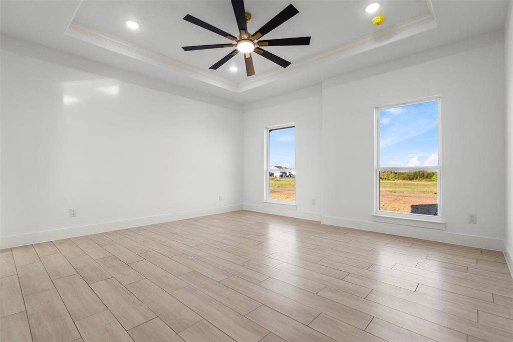 Tray ceiling with recessed lighting, ceiling fan with light fixture, wood-finish flooring, and two windows