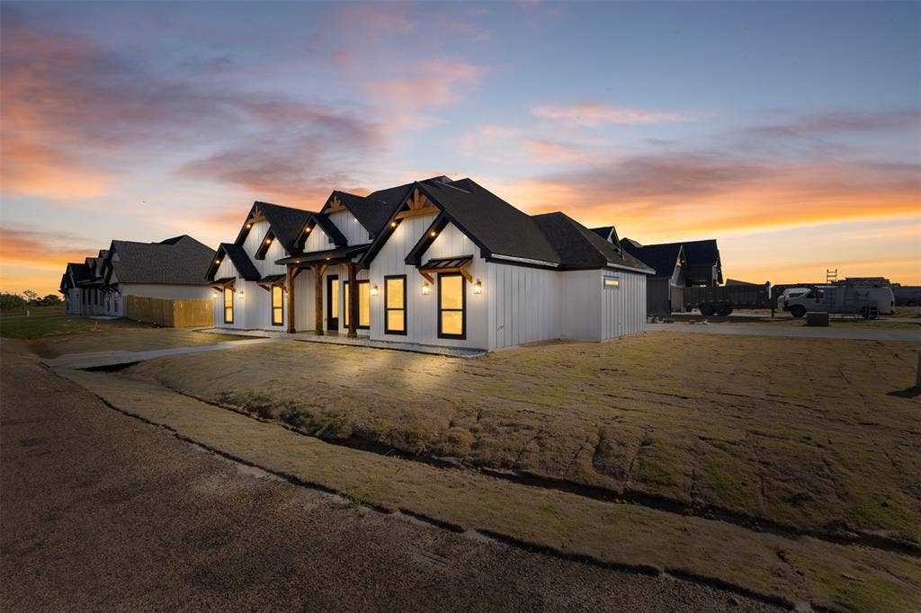 Modern farmhouse exterior with white vertical siding, black-framed windows, dark roofing, and exposed wood structural accents