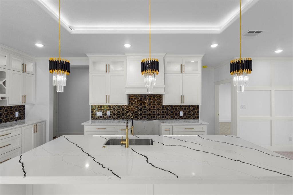 Kitchen featuring a large island with a countertop, gold-finish faucet, and three decorative pendant lights