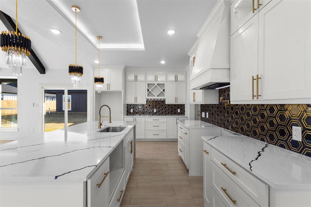 Spacious kitchen with white cabinetry, black and gold hexagonal tile backsplash, white countertops with dark veining, and wood-finish flooring