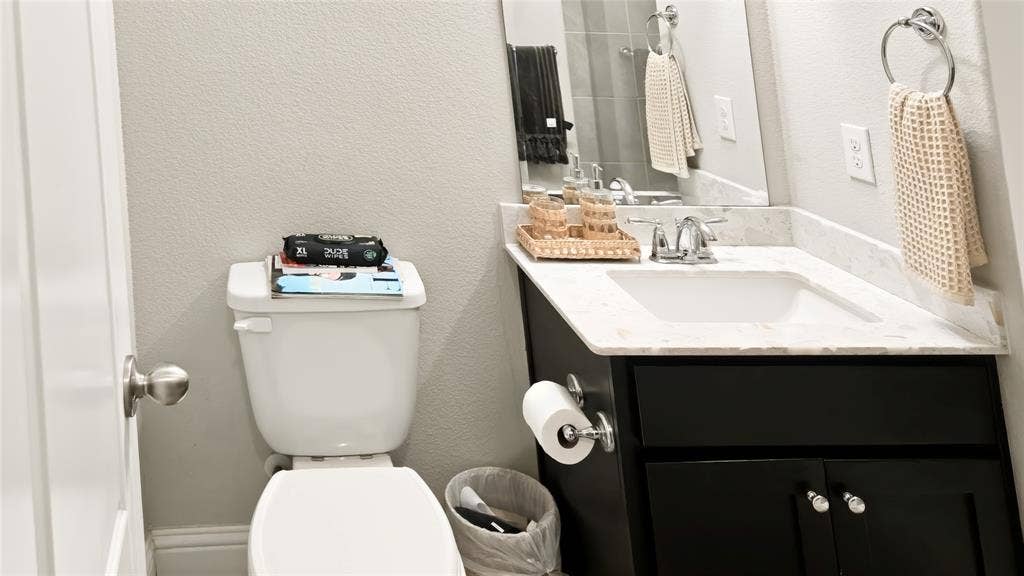 Black cabinetry, white composite countertop with integrated sink, dual-handle chrome faucet, wall-mounted mirror, and wall-mounted ring towel holder