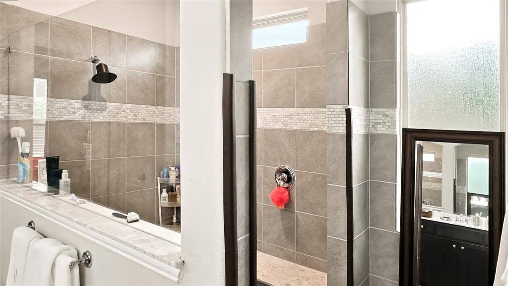 Walk-in shower featuring large-format stone-finish wall tiles, decorative mosaic tile accents, a glass enclosure, and an overhead rainfall showerhead
