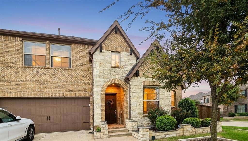 Two-story brick exterior featuring herringbone masonry accents, arched stone entryway, raised stone flower beds, and a multi-car garage