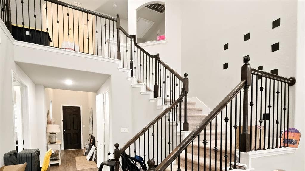 Foyer featuring a two-story ceiling, staircase with dark wood handrails and black metal balusters, and a solid black entry door