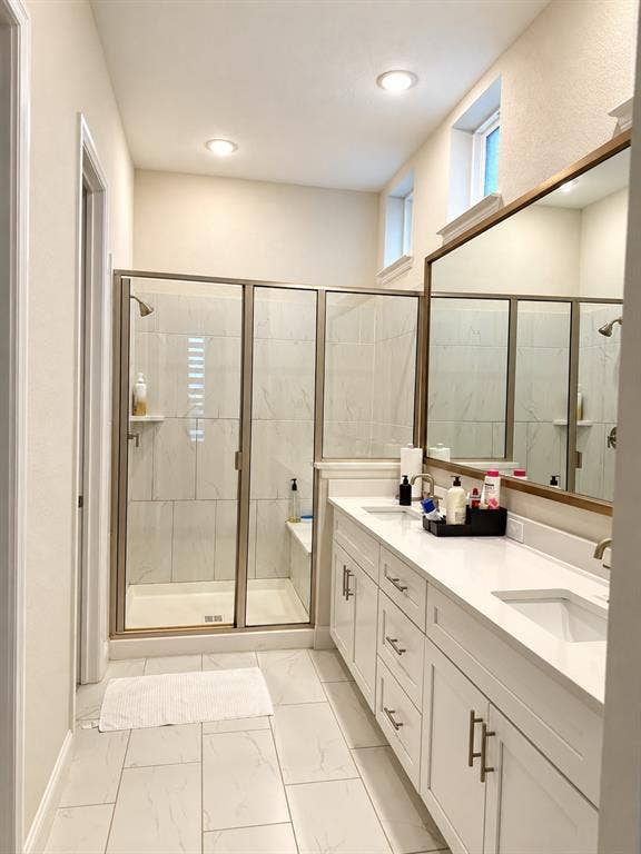 10755 Wells Branch Road, Frisco, TX 75035 Spa-inspired primary bathroom featuring a frameless glass-enclosed shower with tile surround, dual vanity with white cabinetry and quartz countertop, large mirror with integrated lighting, recessed ceiling lights, and tile flooring throughout