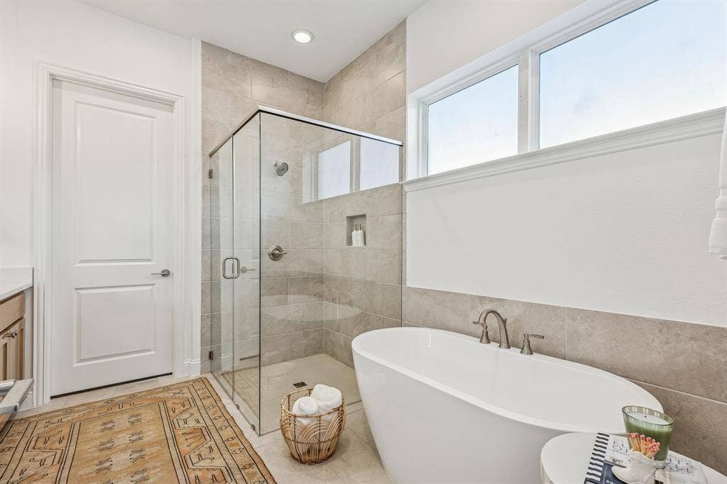 Freestanding soaking tub, walk-in shower with glass enclosure, tile walls, and recessed lighting