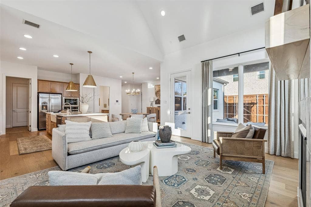 Open-concept living area featuring vaulted ceilings, wood-finish flooring, recessed lighting, and a kitchen with an island and stainless steel appliances