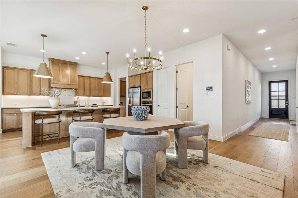 Open-concept layout featuring light wood-finish flooring, a kitchen island with seating, recessed lighting, and a dark-framed glass paneled door