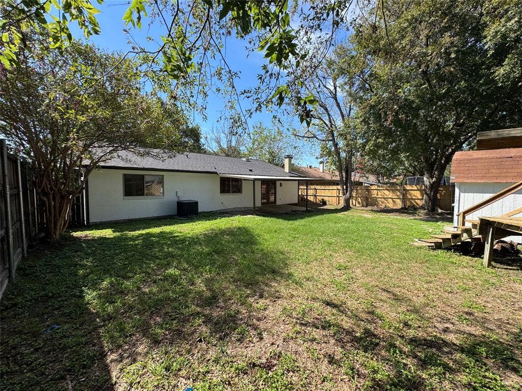 Expansive backyard featuring a manicured lawn, established trees, and a wooden privacy fence