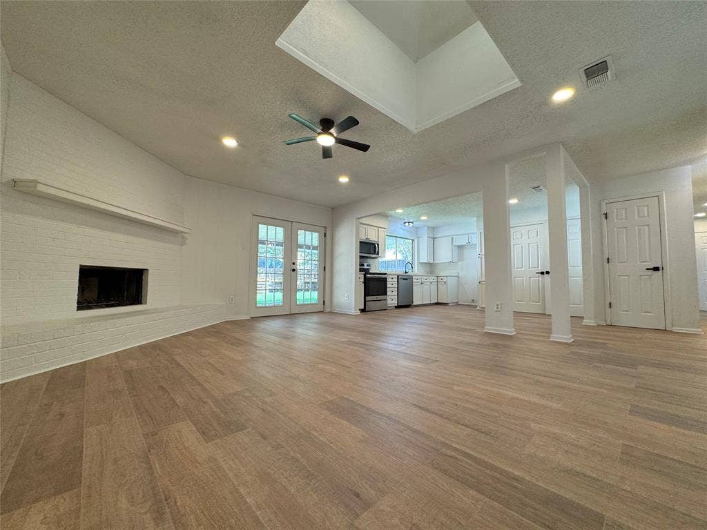 Spacious living area featuring wood-finish flooring, a white brick fireplace, and dual French doors
